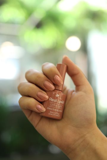 Mão segurando um esmalte rosa-nude
